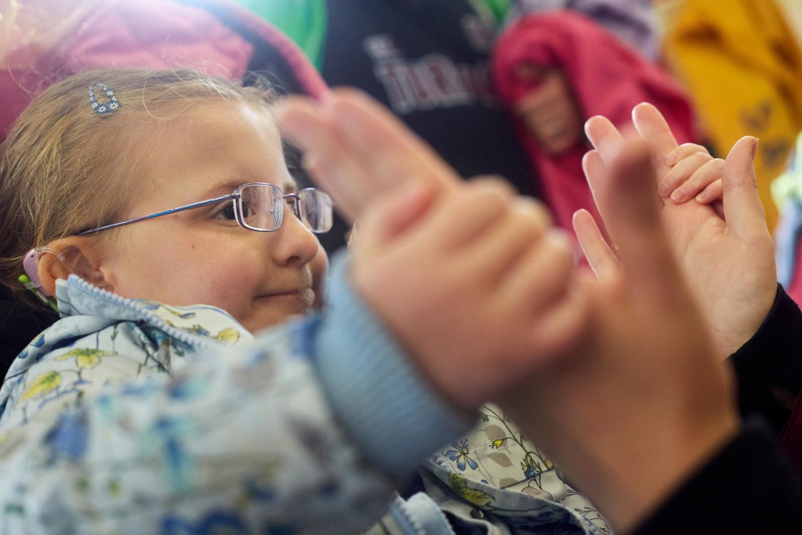 Small child with glasses playing with an adult's hands.