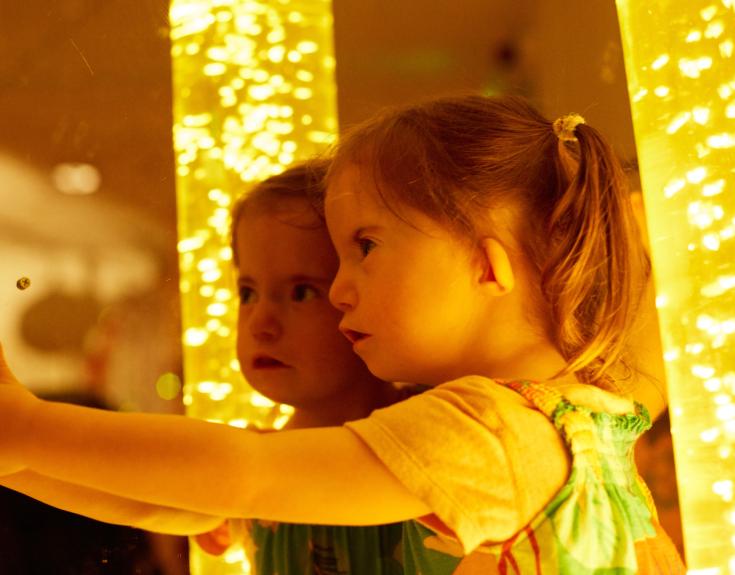 Young child with Down's syndrome standing against a mirror with sparkly lights behind them.