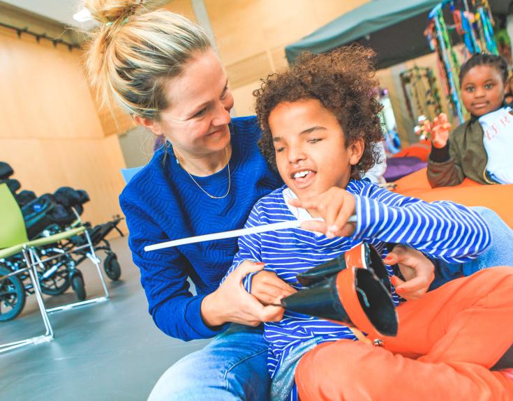 Woman with visually impaired child playing agogô bells.